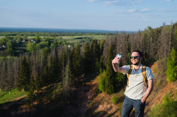 Fototapeta na wymiar Young stylish man with a beard wearing sunglasses makes selfie on the canyon cliff
