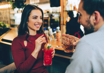 Beautiful girl sitting in the club with ac guy. She holds a glass of cocktail in her hands. She is...