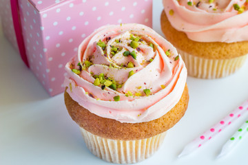 Decorated pink cup cakes with pistachio nut sprinkles - Birthday background with gift and unlit candles