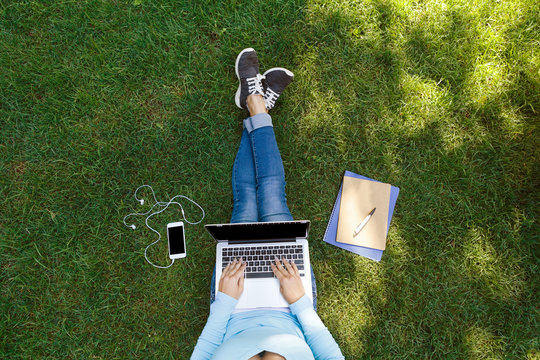 Top view of female student sitting in park with laptop