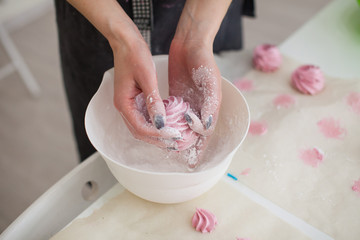Obraz na płótnie Canvas Woman's hands Sprinkling with Icing Sugar a Zephyr . Confectioner Sprinkles Powdered Sugar on pink crimson Marshmallow
