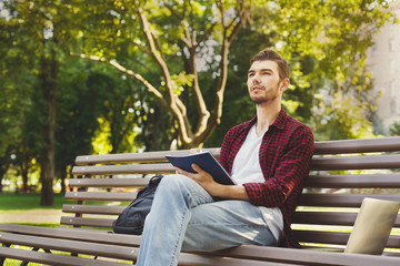 Young man thinking with a copy-book outdoors