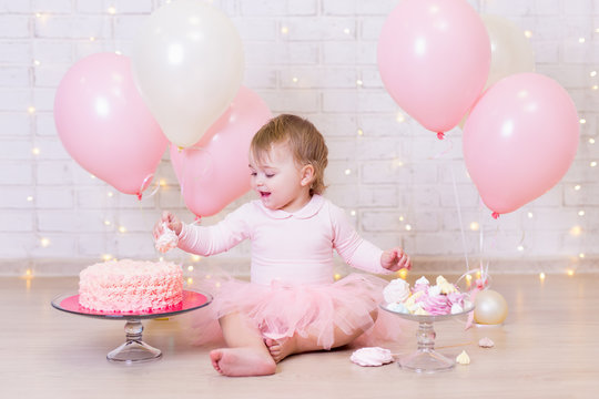 first birthday party concept - funny little girl eating cake over brick wall background with lights and balloons