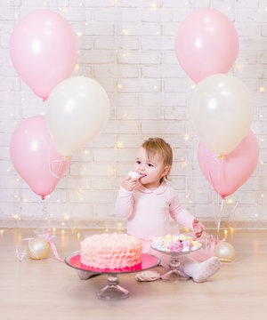 birthday party concept - cute little girl eating cake over brick wall background with lights and balloons