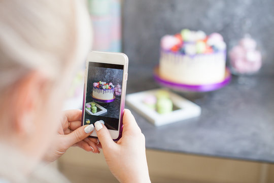 Confectioner makes a photo on the phone. On the cake there are  berries blueberries and strawberries, purple and green macaroons