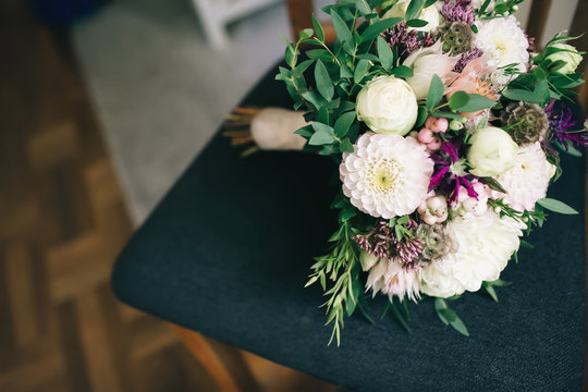 Rustic wedding bouquet with white dahlias, peonies, and greens on a dark chair. Artwork