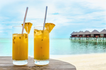 Drinks with a straw on a wooden table on the background of a sandy beach and houses on the water