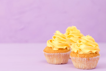 Cupcakes decorated with yellow cream on violet pastel background for greeting card with copyscape.