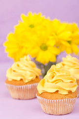 Cupcakes decorated with yellow cream and chrysanthemums on violet pastel background for greeting card with copyscape.