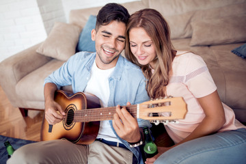 Lovely young couple playing guitar at home