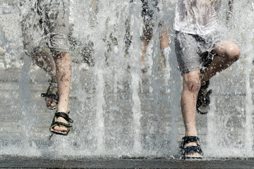 Two boys jumping over fountain streams. Legs