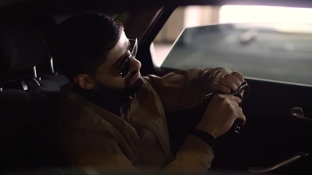 calm armed man is cleaning his gun inside a car in a parking area, he is looking intently on pistol