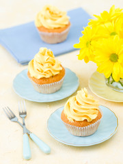 Cupcake with yellow cream decoration and bouquet of yellow chrysanthemum in small glass.