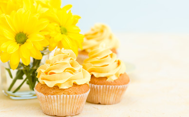 Cupcake with sweet yellow cream decoration and bouquet of yellow chrysanthemum in small glass