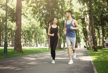 Young couple jogging in green park, copy space
