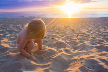Fototapeta na wymiar Baby plaing in sand on the coast of Baltic sea during sunset