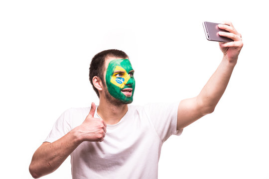 Fan support of Brazil national team take selfie on the phone with painted face isolated on white background