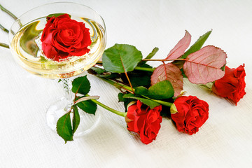 red rose in a glass with champagne and red roses on a table