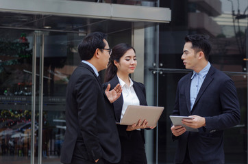 group of business people in suit talking and reading information about finance news in laptop computer together standing in modern city, network technology, internet, successful, teamwork concept