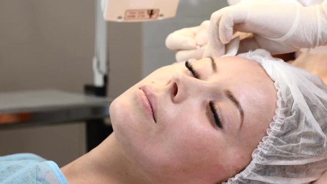 Healtcare clinic. Young female client gets thread face lifting procedure. Cosmetologist in gloves making face anti-aging to a female face