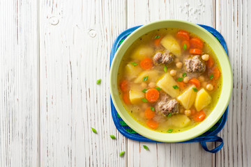 Soup with meatballs, vegetables and chickpea on white wooden table