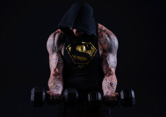 Muscle brutal athlete with tattoos posing in the studio and performing physical exercises