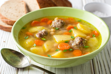 Soup with meatballs, vegetables and chickpea on white wooden table