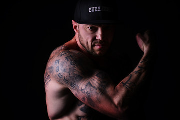 Fototapeta na wymiar Muscle brutal athlete with tattoos posing in the studio and performing physical exercises