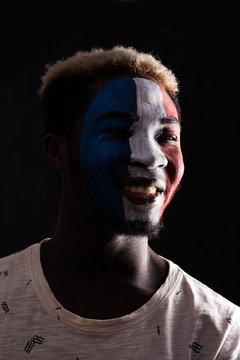 Face portrait of happy afro fan support France national team with painted face isolated on dark background