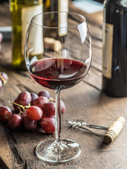 Glass of red wine on the table. Wine bottle and grapes at the background.