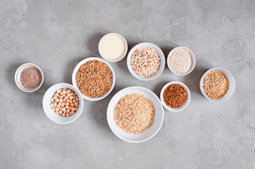 Various cereals and beans in white plates on gray textured table, copy space