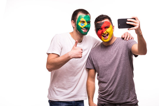 Football fans supporters with painted face of national teams of Brazil and Germany take selfie isolated on white background