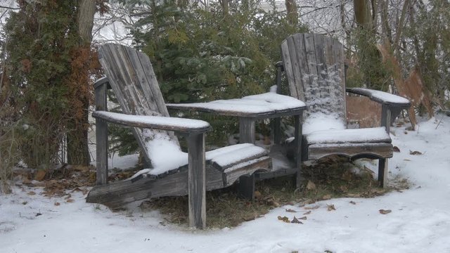 Two wooden chairs and a table covered with snow
