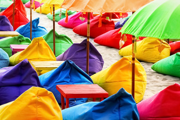 Multicolored bright beach umbrellas, ottomans and tables in the beach cafe. Summer multicolored...