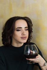 beautiful woman with closed eyes holds a glass of red wine and inhales its aroma