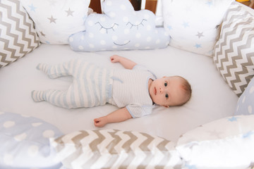 Fototapeta na wymiar Beautiful newborn baby lying in an oval bed with beautiful bumpers in delicate gray, blue, white tones