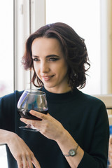 beautiful brunette woman with red wine glass near window