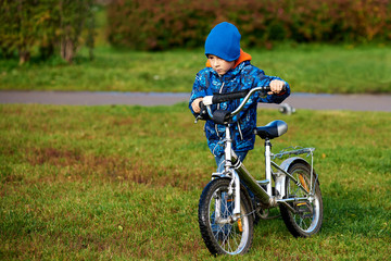 Fototapeta premium Cute european boy is standing near his bicycle in the autumn city park.