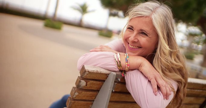 Happy mature woman laughing and relaxing on park bench
