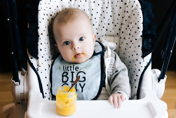 Feeding. Adorable baby child eating with a spoon in high chair. Baby