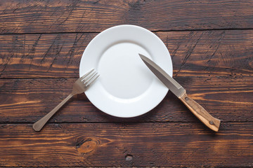 empty plate with knife and fork on dark wooden table
