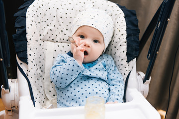 Feeding. Adorable baby child eating with a spoon in high chair. Baby