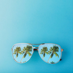 Sunglasses with palm trees reflected in them and space for text, top view
