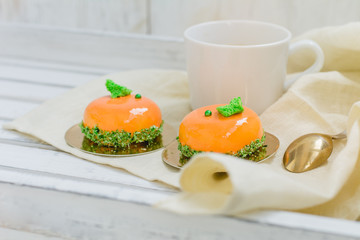 Bright orange mousse cakes and cup of coffee on white wooden tray