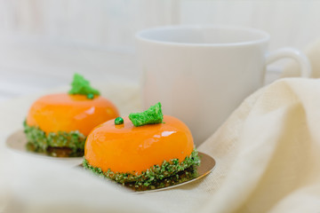Bright orange mousse cakes and cup of coffee on white wooden tray