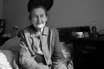 Beautiful 80 plus year old senior woman portrait. Black and white image of elderly worried woman sitting on a bed in a nursing home.