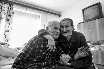 Cute 80 plus year old senior married couple hugging and smiling portrait. Black and white waist up...