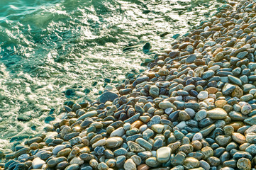 Many colorful stones shinig under the sun on the beach coastline background