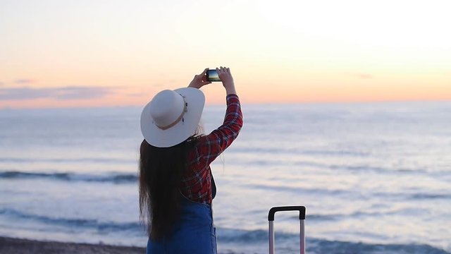 Young woman taking photos on beach during sunset or sunrise