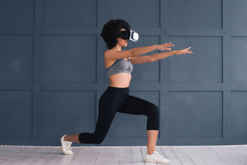 Sport in a new way! Attractive girl with athletic body bending knees to full squat position while wearing the goggles of virtual reality.